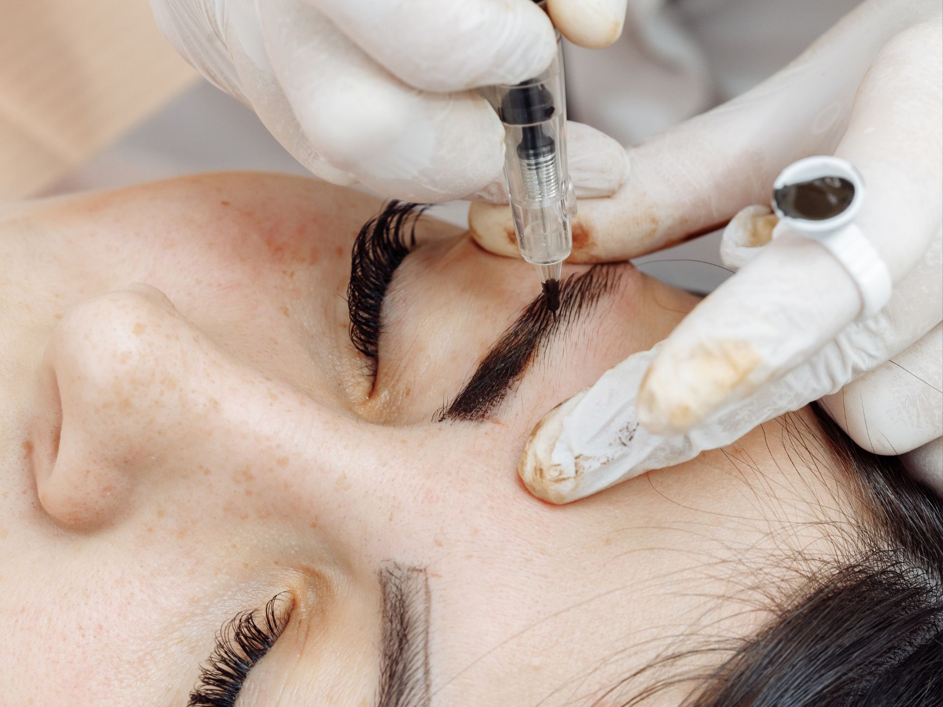 Permanent Makeup Artist applying pigment to eyebrows with permanent makeup pen. 